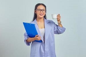 Portrait of smiling young Asian business woman in suit holding document folder and holding mug isolated on purple background photo