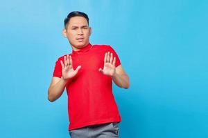Portrait of annoyed young Asian man crossing hands makes stop gesture, demonstrates rejection isolated on blue background photo