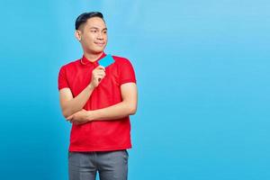Portrait of excited Asian young man showing blank credit card and looking at copy space isolated on blue background photo