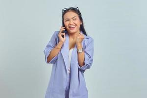 retrato de una joven asiática sonriente celebrando con un teléfono móvil aislado de fondo blanco foto