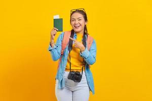 Portrait of cheerful young Asian traveler holding passport boarding pass ticket isolated on yellow background. Passengers traveling on weekends. Air flight travel concept