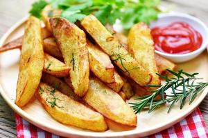 gajos de patata en un plato de madera con hierbas de romero y salsa de ketchup de tomate, cocinando patatas fritas o patatas fritas foto