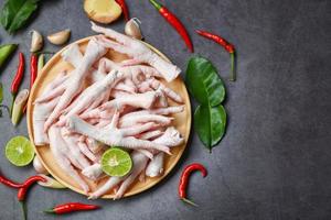 patas de pollo en un plato de madera con hierbas y especias limón chile ajo hojas de lima kaffir, patas de pollo crudas frescas para sopa de comida cocinada en el fondo oscuro de la cocina foto