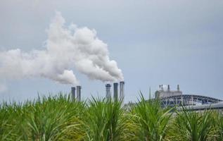 sale humo blanco de las chimeneas o de los tubos de escape de las chimeneas de la fábrica que emiten vapor de agua que se condensa en una nube blanquecina antes de evaporarse, fábrica de azúcar de vapor, generación de electricidad foto