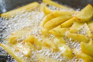 Cooking french fries or fry potatoes in hot oil for potato wedges, Close up fried potatoes in oil on pan photo