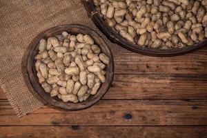 The container on the wood grain table is full of peanuts photo