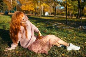 retratos de una encantadora chica pelirroja con una cara linda. chica posando en el parque de otoño con un suéter y una falda de color coral. la niña tiene un estado de ánimo maravilloso foto