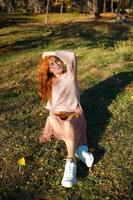 retratos de una encantadora chica pelirroja con una cara linda. chica posando en el parque de otoño con un suéter y una falda de color coral. la niña tiene un estado de ánimo maravilloso foto