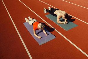 pareja joven haciendo deporte en el estadio acostado en colchonetas de yoga foto