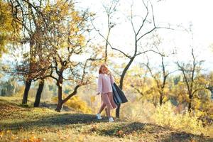 retratos de una encantadora chica pelirroja con una cara linda. chica posando en el parque de otoño con un suéter y una falda de color coral. la niña tiene un estado de ánimo maravilloso foto