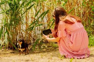 A girl is filming a dog. A teenage girl takes a picture of her black Chihuahua dog outdoors. photo