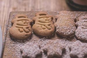 Snowman shaped freshly baked powdered cookies lying on cutting board. photo