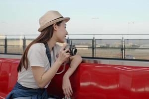 Beautiful Asian female tourist sits in a red seat, traveling by train, taking snapshot photo, transporting in suburb view, enjoy passenger lifestyle by railway, happy journey vacation. photo