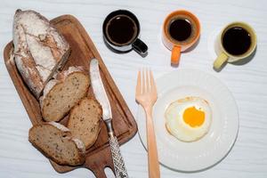 fried egg in plate bread slice in cutting board have espresso coffee on white table.