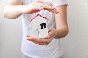 mano de mujer sosteniendo casa modelo de juguete aislada sobre fondo blanco. concepto de hogar de ensueño de seguro de propiedad de hipoteca de bienes raíces. oferta de compra casa de alquiler, vida familiar, negocios inmobiliarios. foto