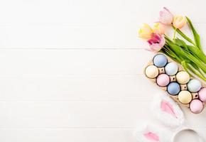 fondo de pascua con huevos, tulipanes y orejas de conejo sobre fondo de madera blanca, vista superior plana foto