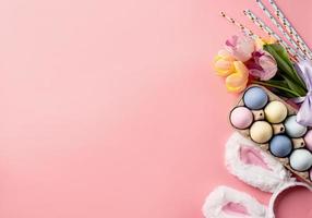 easter background with eggs, bunny ears and tulips on pink backdrop, top view flat lay photo