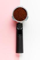 Espresso machine filte holder with ground coffee on pink and white background. photo