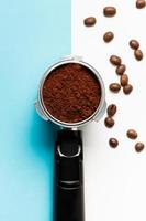 Espresso machine filter holder with ground coffee and coffee beans on blue and white background.