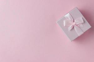 Pink gift box with ribbon tied bow on pink background. Top view photo
