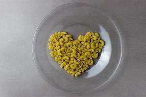 un puñado de pasta seca en forma de corazón sobre un plato transparente sobre una mesa de cocina gris foto