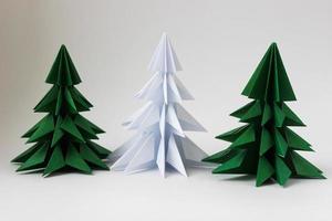 Two origami green christmas tree and white one on white background. photo
