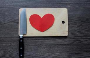 cuchillo con un corazón de papel en una tabla de cortar foto