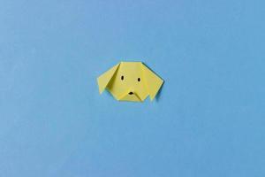 The dog's head is folded from yellow paper in the technique of origami with painted mustache. In center of the blue background. Concept of love dogs, pets, pastime, hobbies, activities with children. photo