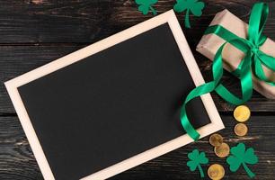 Clover shamrock, gold coins and gift with green ribbon on a brown wooden background. Festive composition. photo