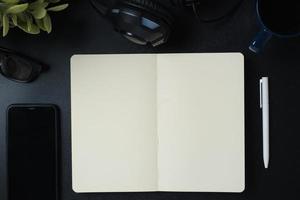 escritorio de trabajo de vista superior con libreta abierta, auriculares y teléfono móvil en el fondo de la mesa negra foto