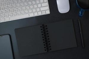 top view working desk with keyboard headphone and open notebook on black table background photo