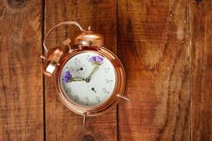 Vintage alarm clock made from gold metal with blue flowers instead of clock's hands on wooding surface. Spring time photo