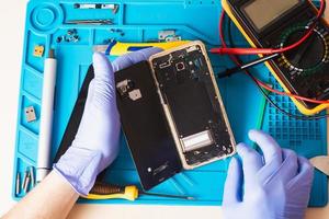 el artesano en guantes de goma repara o repara un teléfono móvil en una alfombrilla de goma especial para reparar. vista desde el interior foto