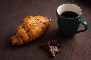deliciosos croissants crujientes, chocolate, café caliente en la taza azul en el plato sobre la mesa oscura. sabroso desayuno