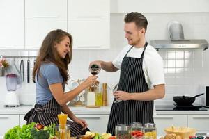 pareja joven bebiendo vino durante la cocción de los alimentos foto