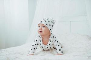 Newborn baby dressed in a white suit and black stars is a white soft bed in the studio photo