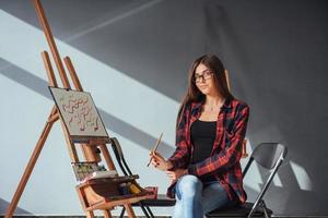artista de pelo oscuro que sostiene un pincel en la mano y dibuja un cuadro sobre lienzo. piensa que se basa en foto