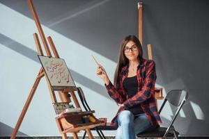 Dark-haired artist holding a brush in his hand and draws a picture on canvas. Thinks that draw on photo