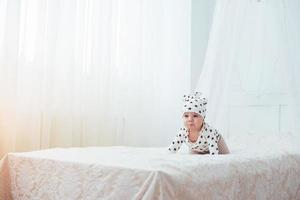 bebé recién nacido vestido con un traje blanco y estrellas negras es una cama blanda blanca en el estudio foto