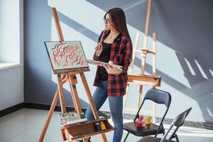 una pintora creativa y pensativa pinta un cuadro colorido sobre lienzo con colores al óleo en el taller. foto