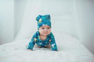 Newborn baby dressed in a green suit lying on a soft bed in a white studio. photo