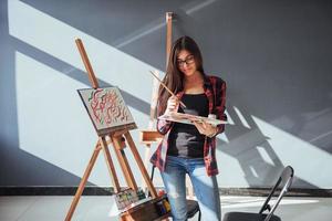 Creative pensive painter girl paints a colorful picture on canvas with oil colors in workshop photo