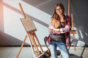 artista de niña bonita pinta sobre lienzo pintando en el caballete. fondo negro de estudio. pelo largo, morena. foto