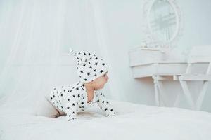 Newborn baby dressed in a white suit and black stars is a white soft bed in the studio photo