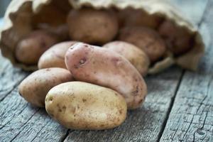 Potatoes which just fell out of the burlap sack lying on the wood boards photo