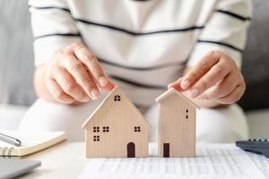 la mujer está decidiendo elegir una casa con un modelo de casa pequeña de madera, planeando comprar una propiedad. elegir lo que es mejor. conceptos de préstamos hipotecarios. foto
