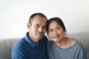 retrato de una pareja madura asiática sentada en la sala de estar. esposa y esposo abrazándose, tomados de la mano con felicidad y alegría. concepto de familia de amor, seguridad y seguros foto