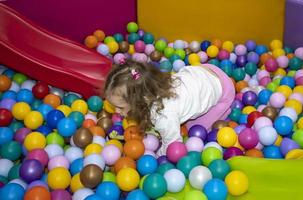 A little girl has fun riding the slides of the sports game complex. Dry Pool with Colored Balls. Children's Sports Exercises. Physical education for children. photo