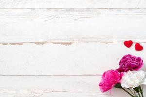 May mothers day concept photography - Beautiful carnations and hearts shape with white empty card isolated on a bright wooden table, copy space, flat lay, top view, mock up photo