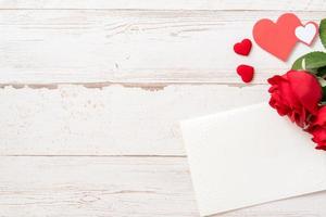 Greeting concept - Beautiful roses and hearts shape with white empty card isolated on a bright wooden table, copy space, flat lay, top view, mock up photo